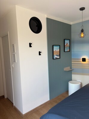 Une chambre à coucher avec un lit, un élément de décoration murale rond, deux tableaux encadrés, un luminaire suspendu et une poubelle blanche.