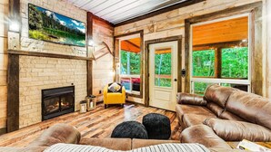 Un salon chaleureux avec une cheminée, un canapé en cuir et une grande fenêtre donnant sur la forêt.