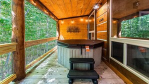 Une terrasse en bois avec un jacuzzi, des rampes en bois et une vue sur la forêt.