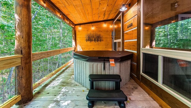Une terrasse en bois avec un jacuzzi, des rampes en bois et une vue sur la forêt.