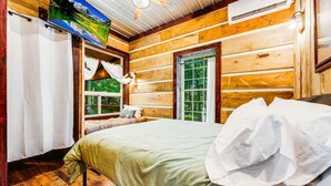 Une chambre dans une cabane en bois, avec un lit, une fenêtre et un ventilateur de plafond.