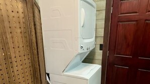 Une petite buanderie équipée d’un lave-linge et d’un sèche-linge superposés, d’une porte en bois et d’un plancher en bois.