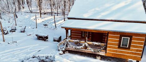 A wooden cabin with a porch, surrounded by snow-covered trees.