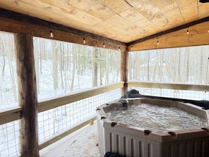 Een hottub in een houten hutje met uitzicht op een besneeuwd bos.