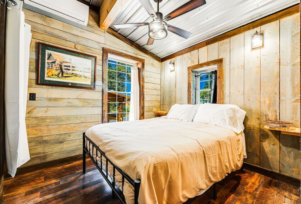 Une chambre à coucher avec un lit, des murs en bois, un ventilateur de plafond et une fenêtre.