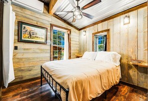 A bedroom with a bed, wooden walls, a ceiling fan, and a window.