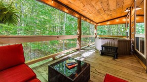 Terraza de madera con vistas a un bosque, chimenea y asientos rojos.