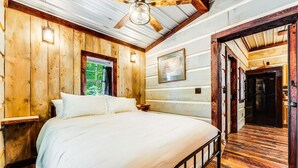 Un dormitorio con paneles de madera, una cama, un ventilador de techo y una puerta que da a otra habitación.