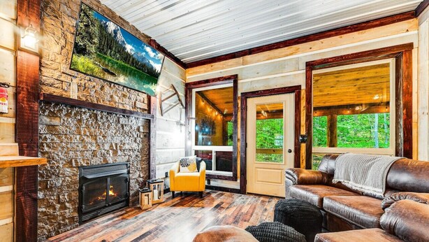 Una sala de estar acogedora con chimenea de piedra, sofá de cuero y un amplio ventanal con vistas al exterior.