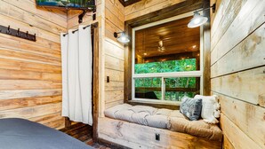 A wooden cabin room with a window seat, a bed, and a view of greenery outside. - EvergreenGrove-2 cabins/4BR (Oakland)