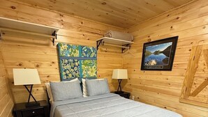 Ett sovrum i en stuga med träpanel, inrett med en säng, två sängbord med lampor, en mönstrad matta och en inramad tavla på väggen.