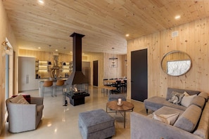 Un interior moderno con techo de madera, chimenea central, comedor y zona de estar acogedora.