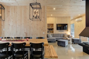 Un interior moderno con un panel de madera, un comedor con mesa y sillas de madera, un sofá gris y una televisión.