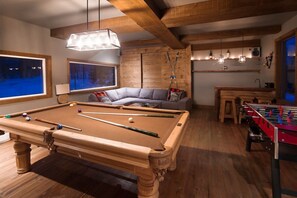 A cozy room with a pool table, a foosball table, a sofa, and a large window with a view of a snowy landscape. - Blue Hill  Pool, spa, game room, mountain view (Morin-Heights)