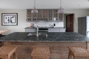 A kitchen with a large island, grey cabinets, pendant lights, and a framed picture on the wall. - Blue Hill  Pool, spa, game room, mountain view (Morin-Heights)