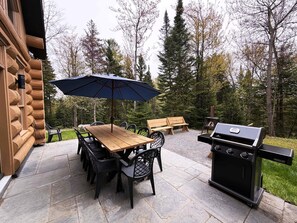 Une terrasse avec une table en bois, des chaises, un barbecue et un parasol.