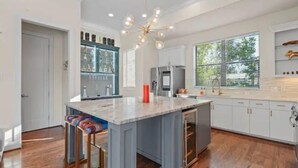 A modern kitchen with a central island, white cabinetry, and a large window providing natural light. - Luxury Midtown Gem : Amazing Rooftop Views (Houston)