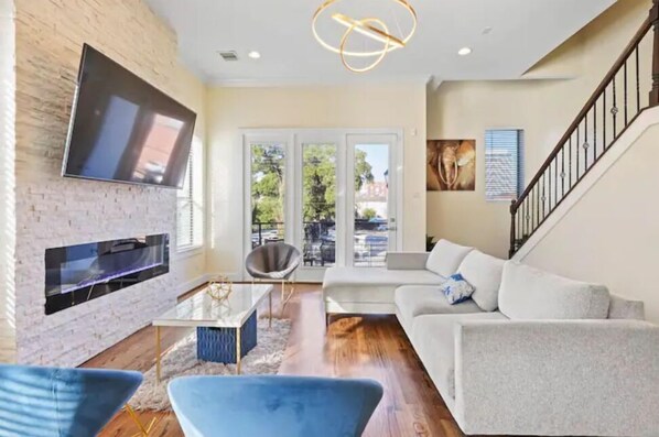 A modern living room with a flat-screen TV mounted on a brick wall, a sofa, a coffee table, and a staircase.