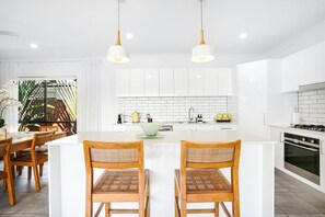 A modern kitchen with white cabinetry, a central island with bar stools, and a dining area with wooden chairs.