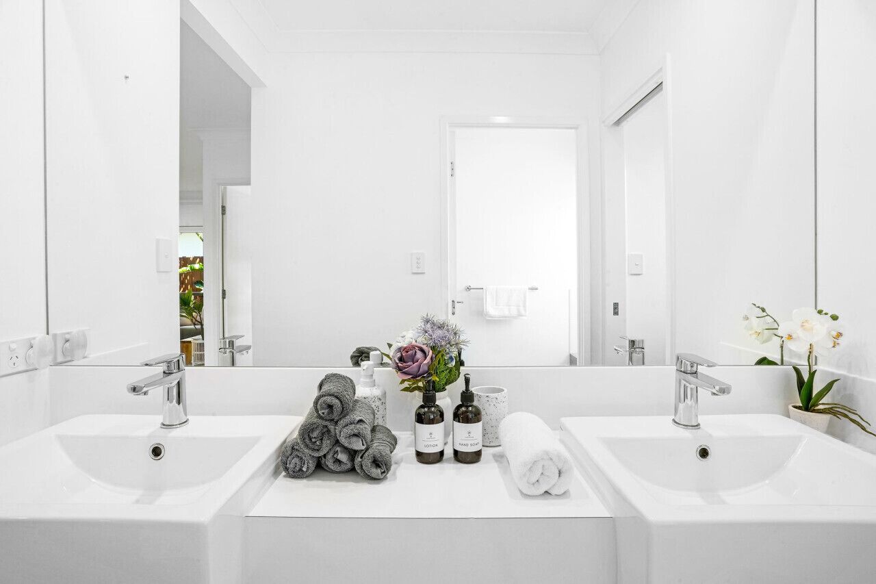 Un baño moderno con dos lavamanos, un espejo grande y artículos de aseo.