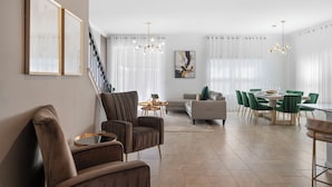 Un vaste salon agrémenté d’un escalier, un coin repas avec des chaises vertes et un lustre moderne.