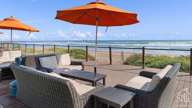 A deck with wicker furniture and orange umbrellas overlooking the beach.