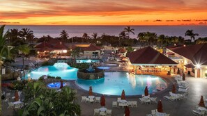 Ett semesterhotell med ett stort poolområde, flera vattenattraktioner och utsikt över havet vid solnedgången.