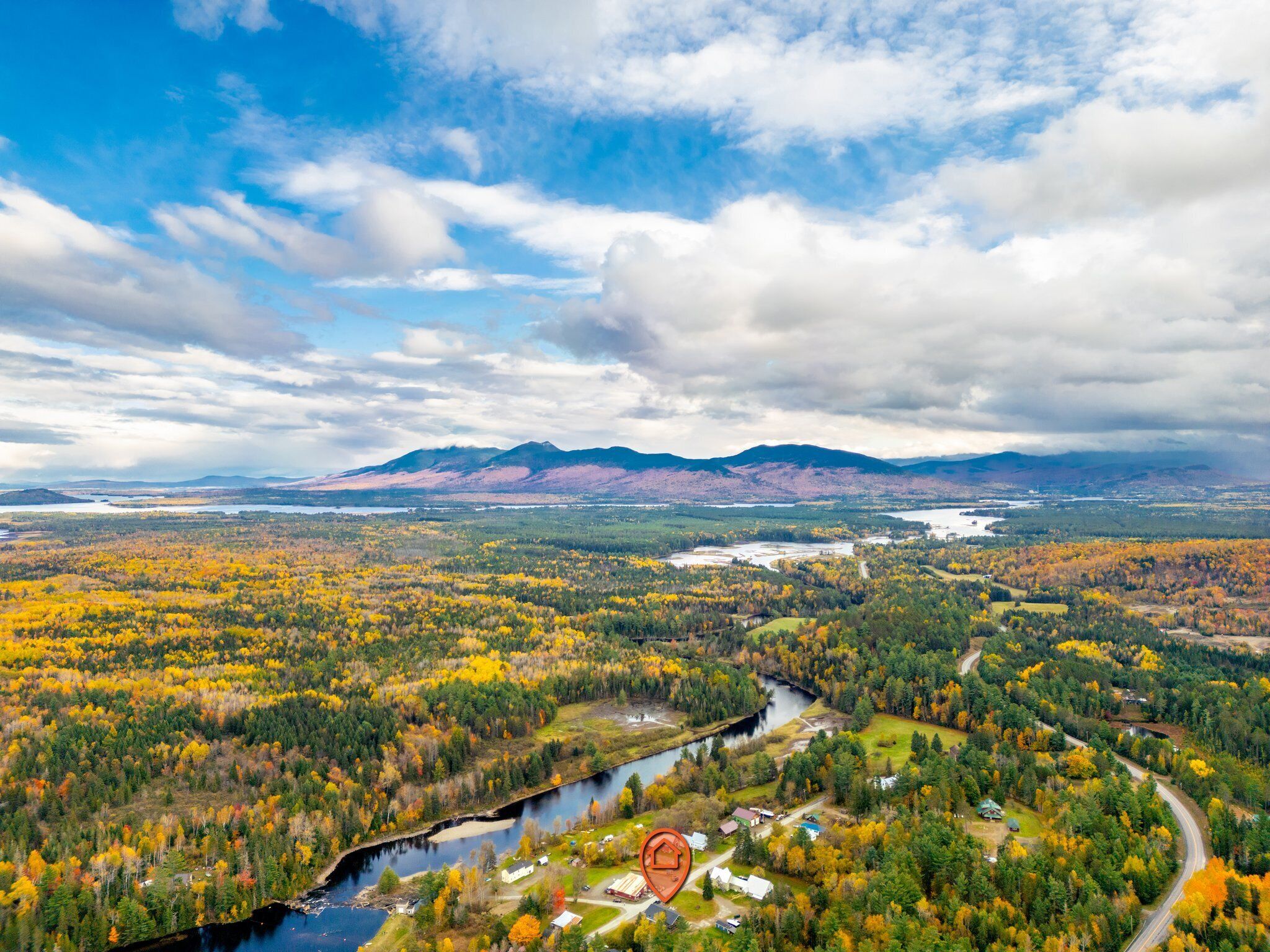 A panoramic view of a valley with autumn foliage, a river, and distant mountains.