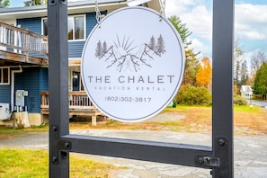 Une enseigne indiquant « The Chalet Vacation Rental », avec une illustration représentant une montagne et un arbre, ainsi qu’un numéro de téléphone.