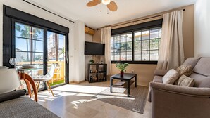 A modern living room with a sofa, a coffee table, a TV, and a balcony with a glass door.