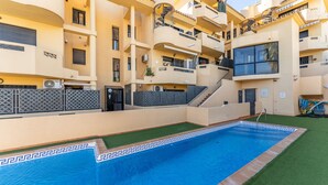 A modern apartment building with a swimming pool, balconies, and a covered outdoor area.