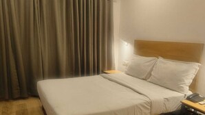 A hotel room with a bed, a nightstand, a chair, and a curtain. - Wishotel Xpress Hotel GK Inn  (Dewas)