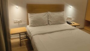 A hotel room with a bed, bedside table, and a nightstand with a phone. - Wishotel Xpress Hotel GK Inn  (Dewas)