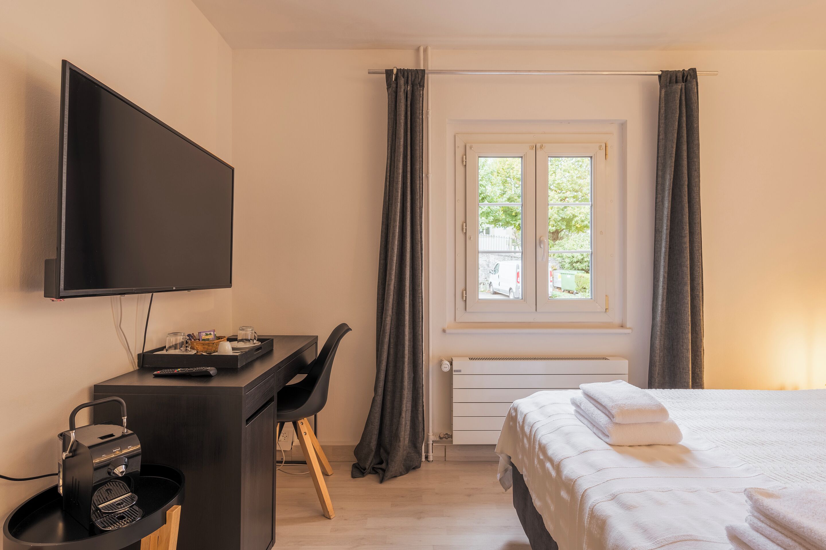 A hotel room with a bed, a desk with a TV, a grill, and a window with curtains.