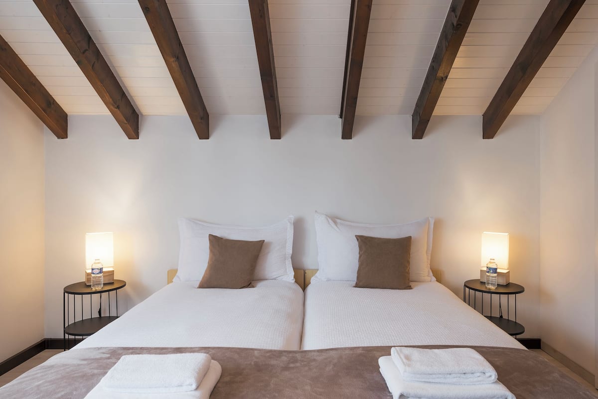 A double bed with white linens and brown pillows, two bedside tables with lamps, and a wooden ceiling.