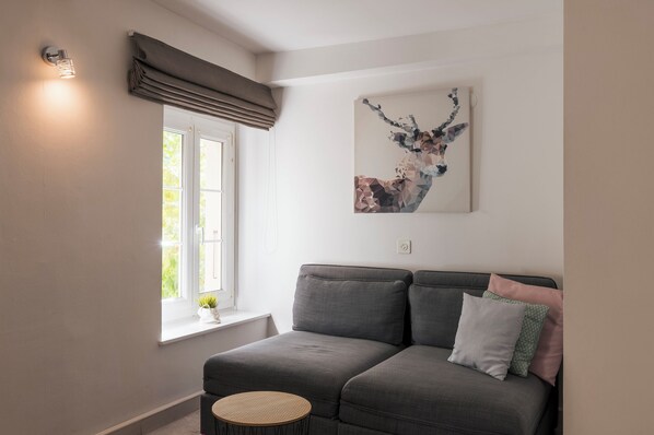 A modern living room with a grey sofa, a small round table, and a window with curtains. - Amanthos Living Nyon (Self Check In) (Duillier)