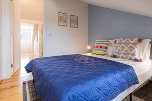 A bedroom with a bed, a blue quilt, two wall-mounted artworks, and a patterned pillow.
