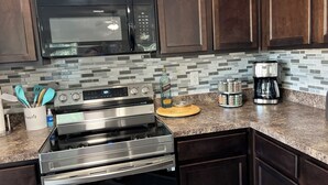 Una cocina con armarios de madera oscura, estufa de acero inoxidable, microondas y cafetera.
