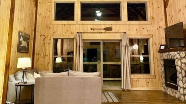 A spacious room with wooden walls, a ceiling fan, a fireplace, and a large window.