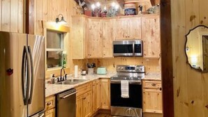 A wooden cabin-style kitchen with a refrigerator, stove, microwave, and wooden cabinets.
