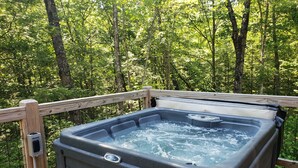 A hot tub on a wooden deck surrounded by a wooden railing, with a control panel on the side.