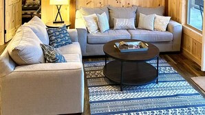 A cozy cabin interior with a wooden interior, a couch, a coffee table, and a sign reading "WHITE HORSE TAVERN".
