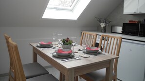 A dining area with a skylight, wooden chairs, a table set for four, and a kitchen with a microwave and washing machine.