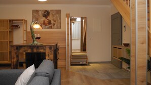 A cozy living room with a wooden floor, a gray sofa, a wooden coffee table with a lamp, and a painting on the wall.