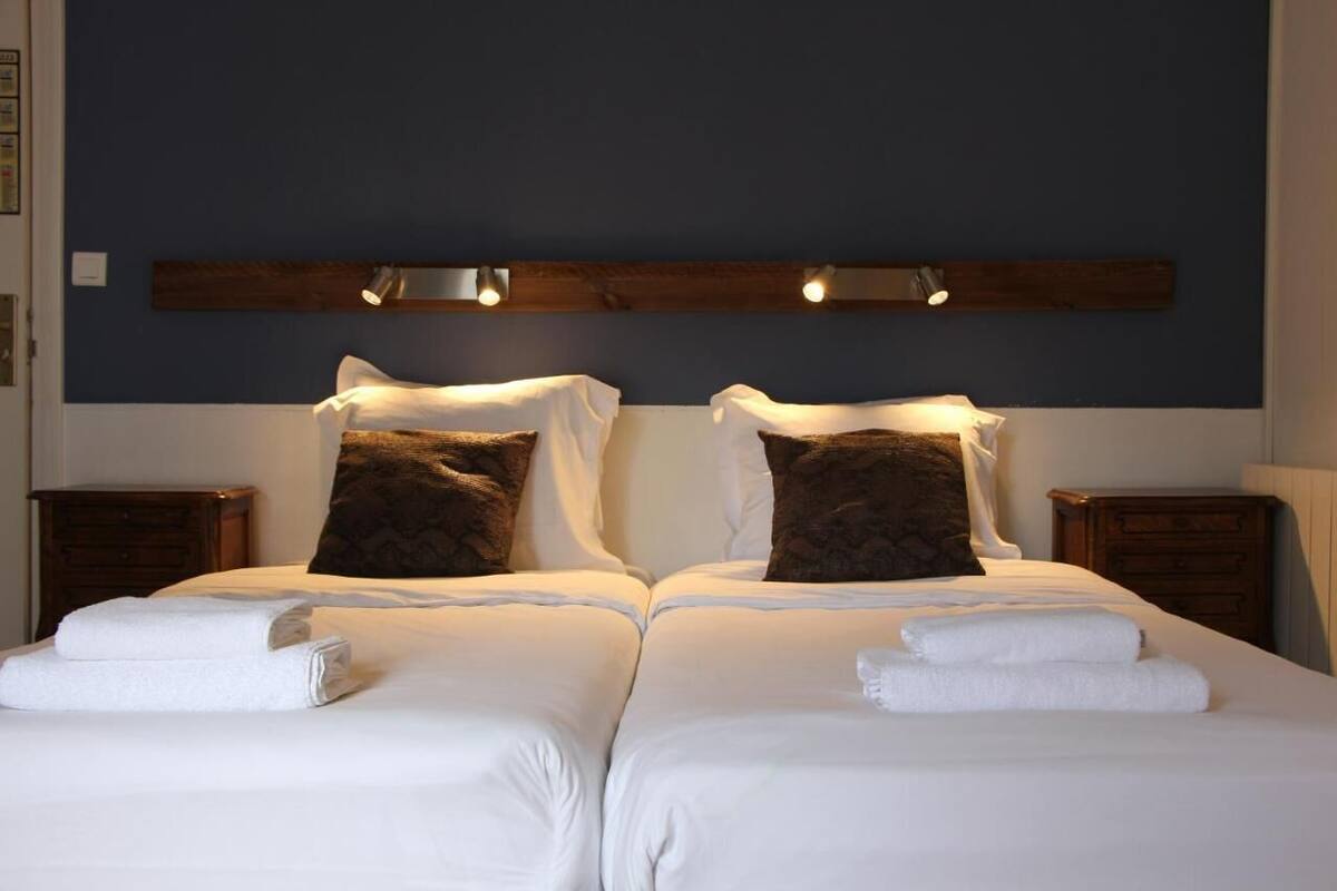 A double bed with white linens and two pillows, a wooden headboard, and two bedside tables with lamps.