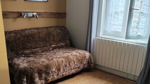 A room with a wooden floor, a brown sofa, a black chair, and a window with curtains. - Hôtel Au Grand Duquesne  (Dieppe)
