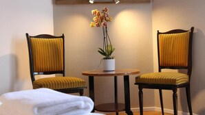 A room with two wooden chairs with yellow upholstery, a small round wooden table with a potted orchid, and a white towel on the floor. - Hôtel Au Grand Duquesne  (Dieppe)
