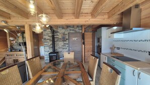 A modern kitchen with a central island, wooden ceiling beams, stone wall, and a built-in stove. - Exceptional Chalet for Rent in La Féclaz – 4 Bedrooms, Sleeps 10** (Les Deserts)
