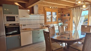 A kitchen with wooden beams, a dining table with wicker chairs, and a view of the outside. - Exceptional Chalet for Rent in La Féclaz – 4 Bedrooms, Sleeps 10** (Les Deserts)