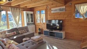 A cozy wooden cabin interior with a sofa, TV, and windows overlooking a scenic view. - Exceptional Chalet for Rent in La Féclaz – 4 Bedrooms, Sleeps 10** (Les Deserts)